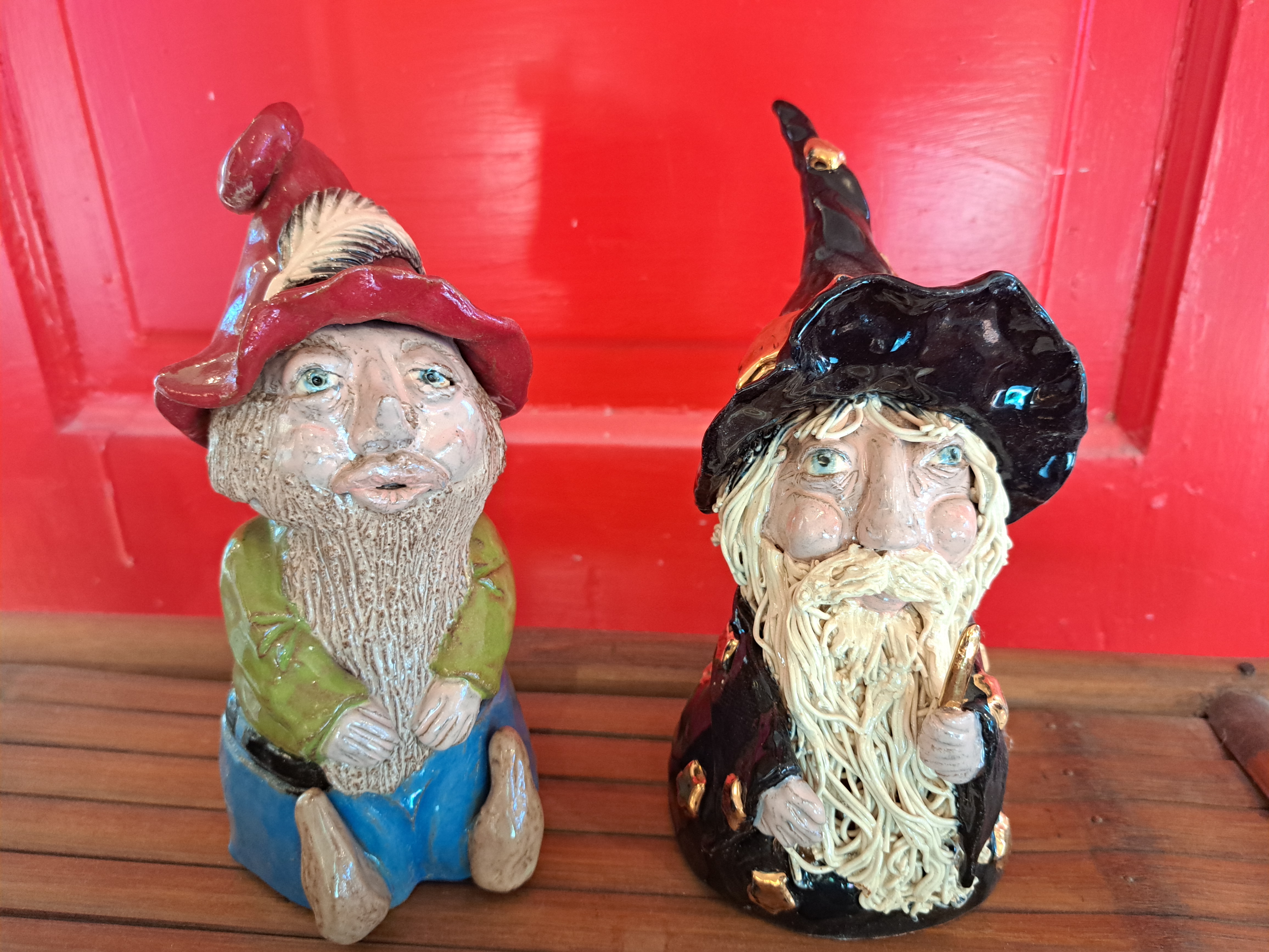 Two gnomes sitting on a wooden table, surrounded by greenery and flowers.