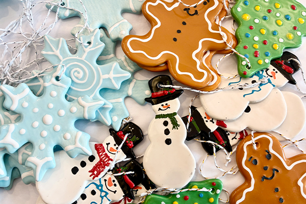 A collection of festive ceramic holiday ornaments shaped like snowflakes, snowmen, gingerbread men, and Christmas trees.