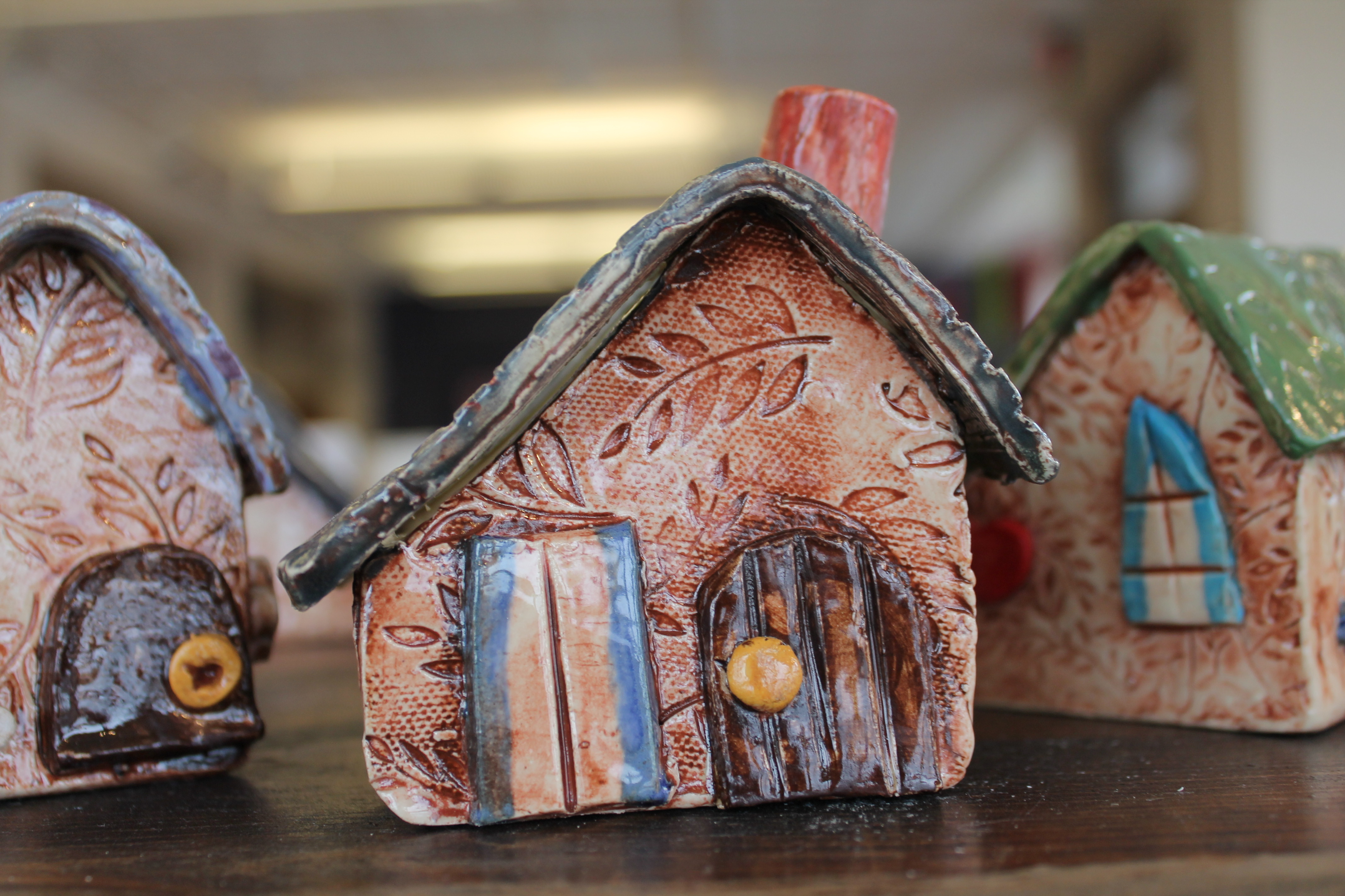 "Handcrafted ceramic miniature houses with intricate designs and vibrant colors, displayed on a wooden surface."