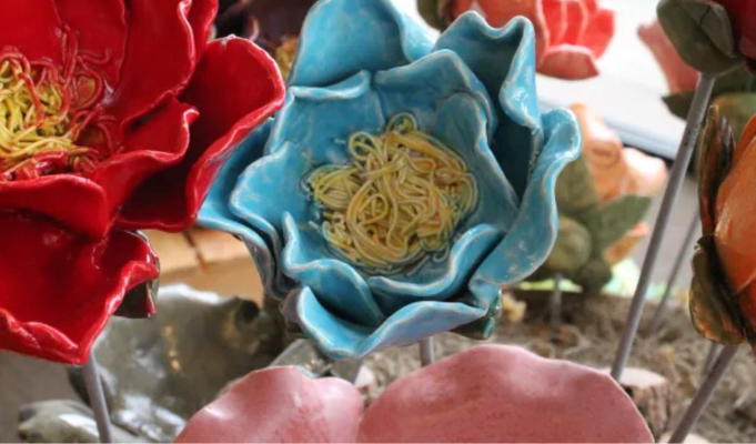 Handcrafted ceramic garden flower in shades of blue displayed with colorful ceramic flowers, showcasing a decorative clay garden art piece created at Sunshine Studios.