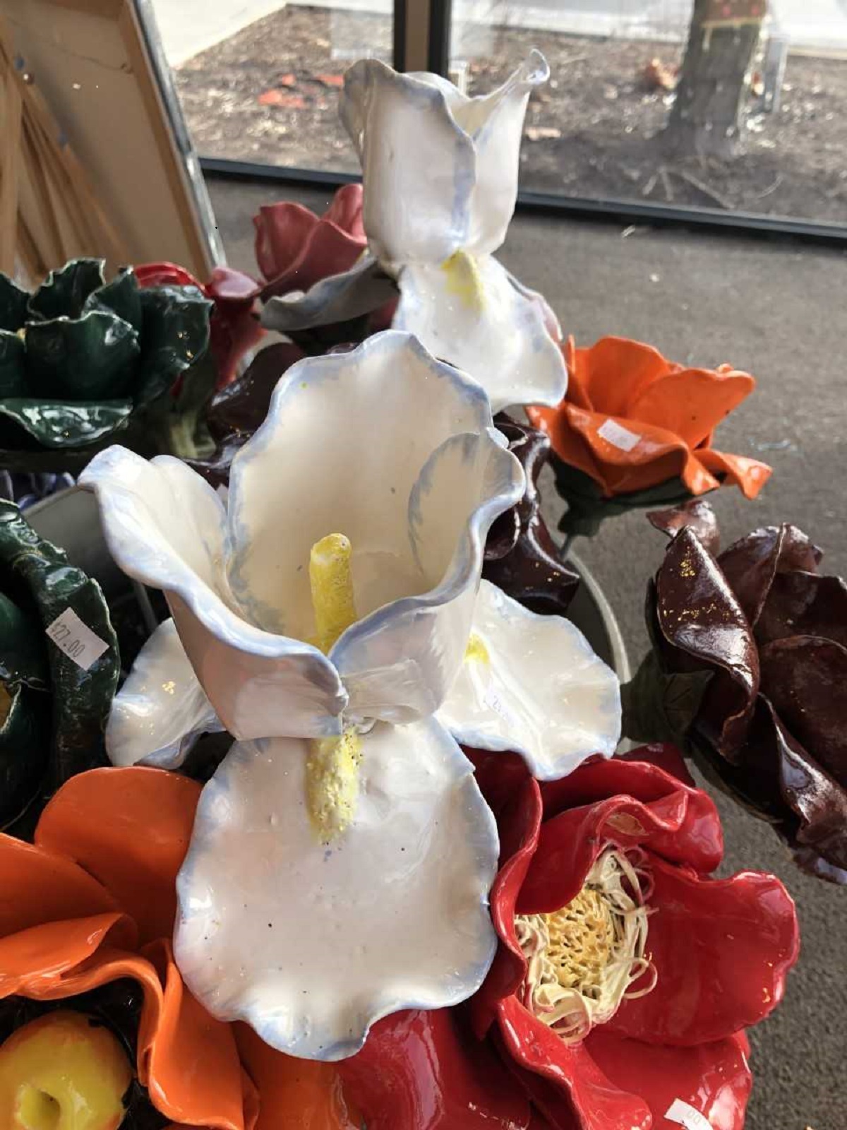 Handcrafted ceramic iris flowers with white petals and yellow centers displayed alongside colorful ceramic garden flowers, created in a Sunshine Studios pottery class.