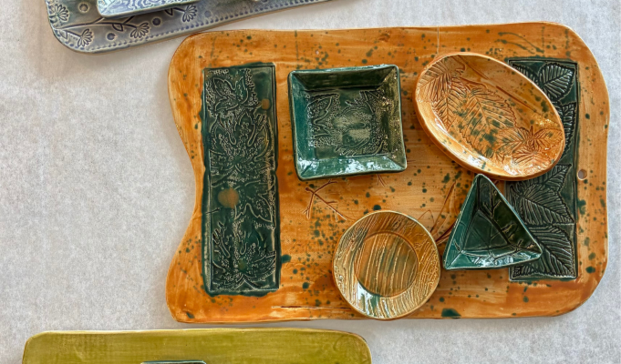Handmade ceramic charcuterie boards with matching serving dishes featuring botanical relief textures and colorful glazes, displayed as functional pottery created at Sunshine Studios.