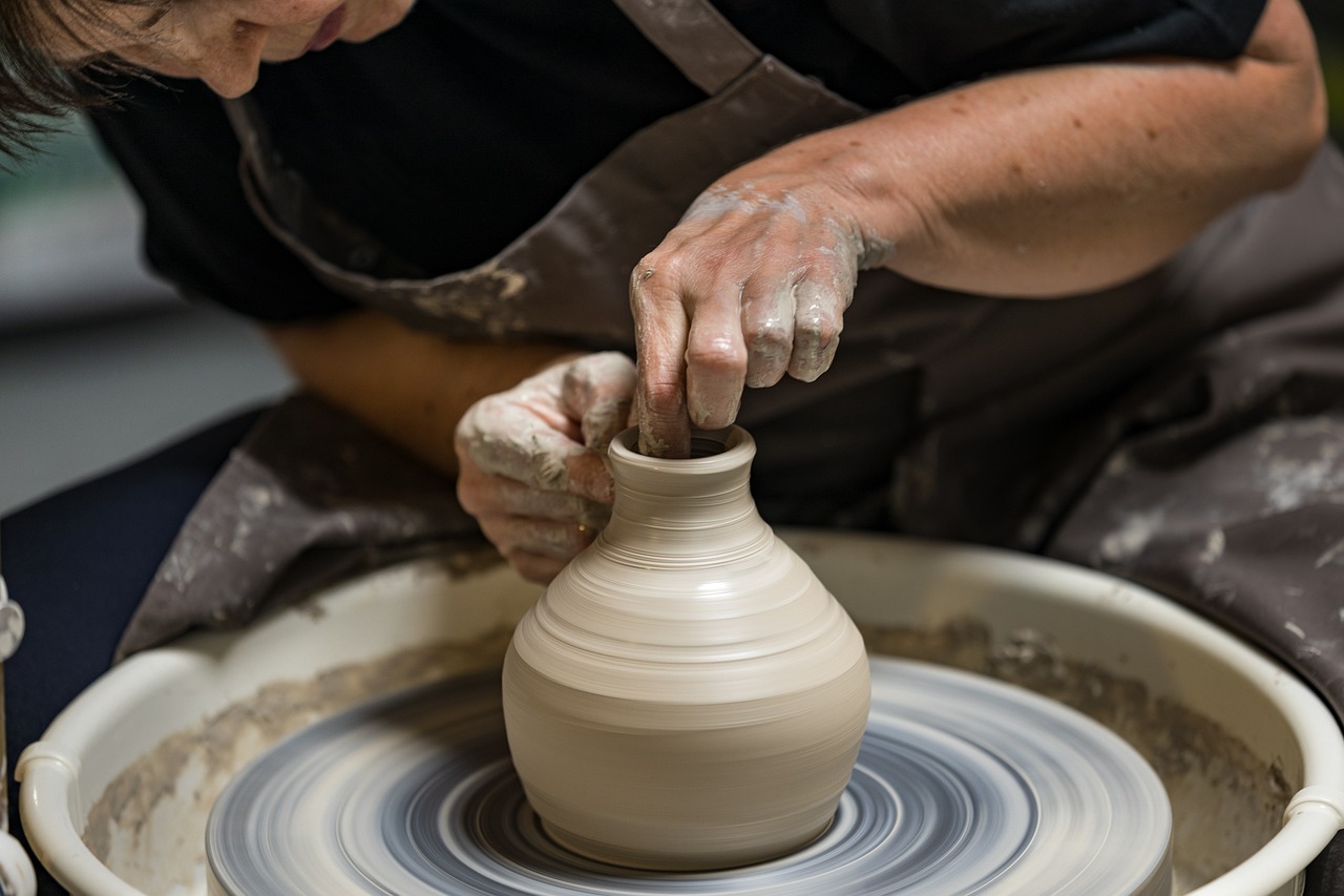 Close-up of a person shaping a clay vase on a pottery wheel, with hands covered in wet clay while wearing an apron.