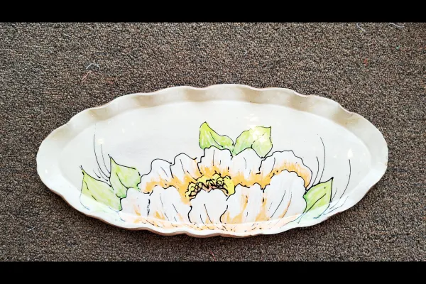 "Handcrafted ceramic platter with a scalloped edge, featuring a floral design painted in yellow, green, and black outlines."