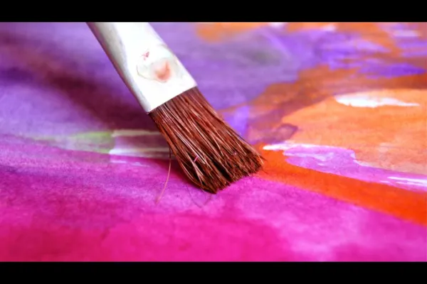 "Close-up of a paintbrush gliding vibrant pink and purple watercolor paint across a canvas, blending colors seamlessly.