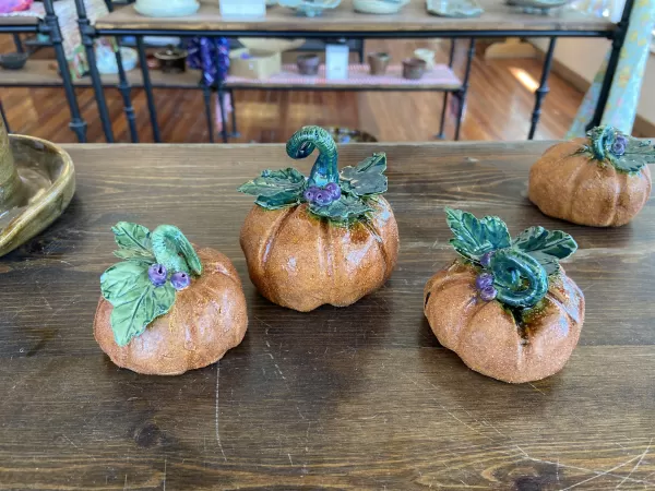 A table with 3 ceramic pumpkins arranged on top.