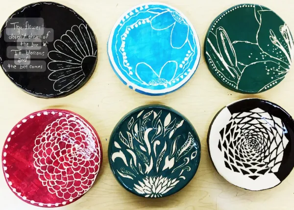 A collection of six beautifully crafted ceramic plates, each featuring intricate sgraffito designs. Patterns range from floral and geometric motifs to inspiring quotes, showcasing creativity and attention to detail. The plates are painted in vibrant colors like red, teal, black, and blu