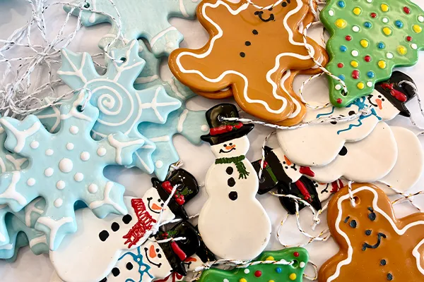 A collection of festive ceramic holiday ornaments shaped like snowflakes, snowmen, gingerbread men, and Christmas trees.