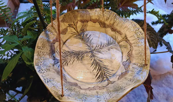 Handcrafted ceramic leaf bowl with carved botanical details hanging among lush greenery at Sunshine Studios, showcasing artwork created through inclusive arts programming.