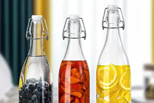 Three glass bottles with swing-top lids are filled with fruit-infused water, displayed on a wooden surface.