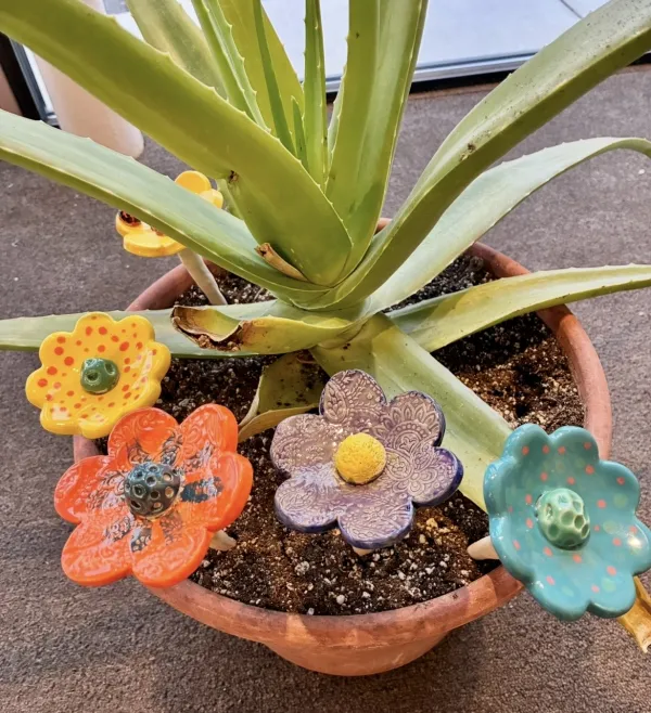 Four handcrafted ceramic bee baths in colorful glazed flower designs created during a Sunshine Studios pottery class, providing a decorative water source for pollinators in the garden.