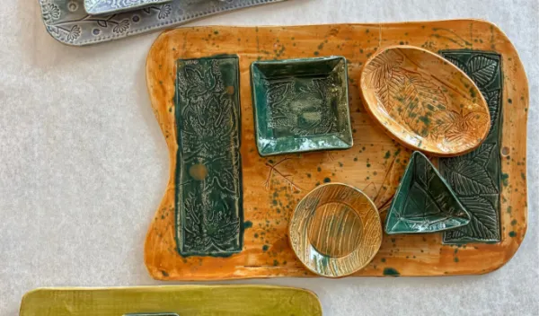 Handmade ceramic charcuterie boards with matching serving dishes featuring botanical relief textures and colorful glazes, displayed as functional pottery created at Sunshine Studios.