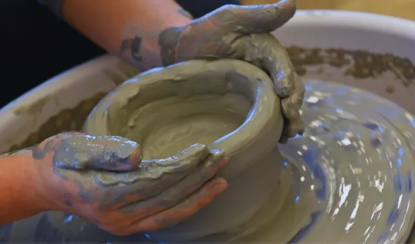 Hands covered in clay shape a ceramic bowl on a pottery wheel during a hands-on pottery class at Sunshine Studios.